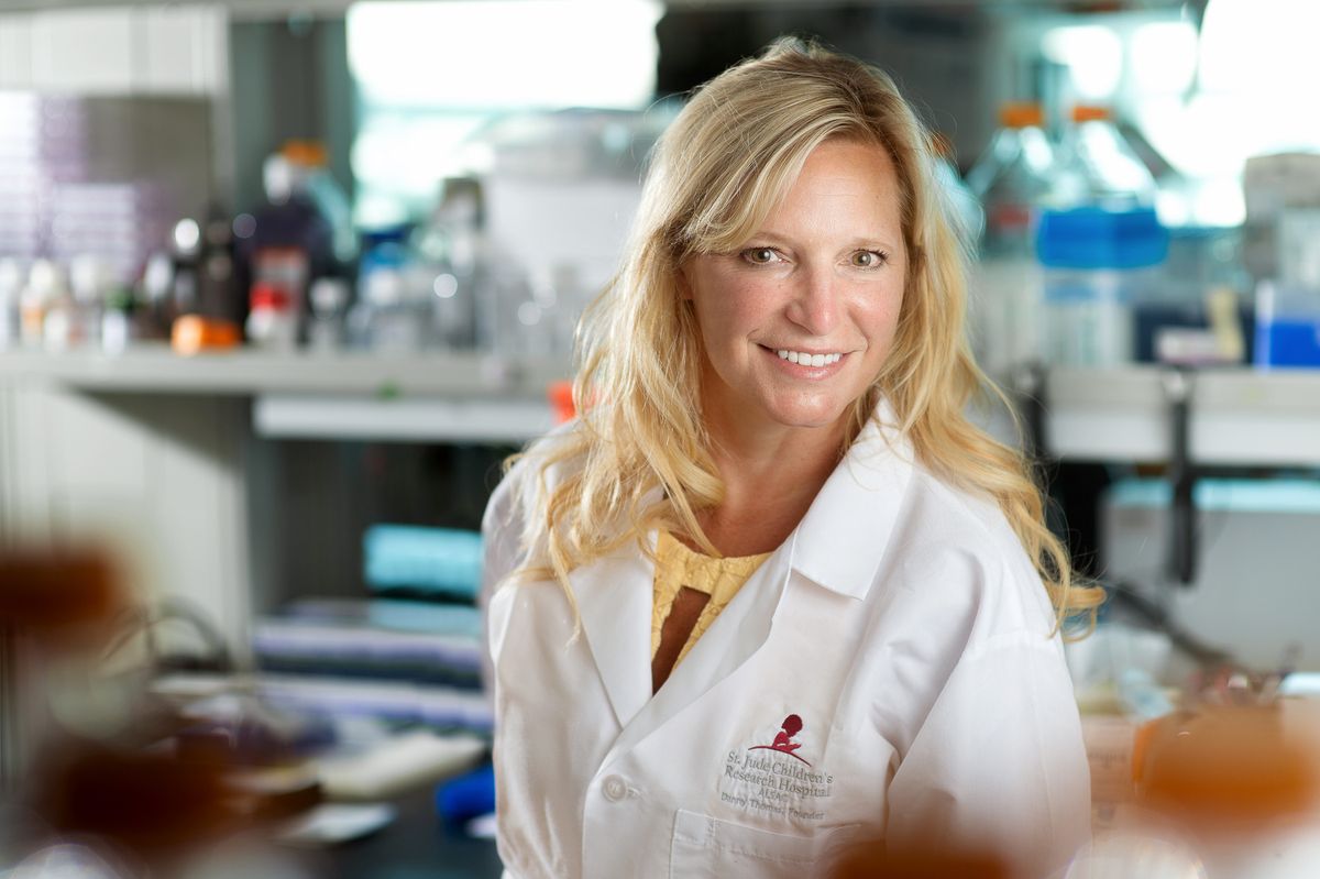 Stacey Schultz-Cherry wears a white lab coat and stands in a laboratory full of research equipment. Stacey Schultz-Cherry wears a white lab coat and stands in a laboratory full of research equipment.