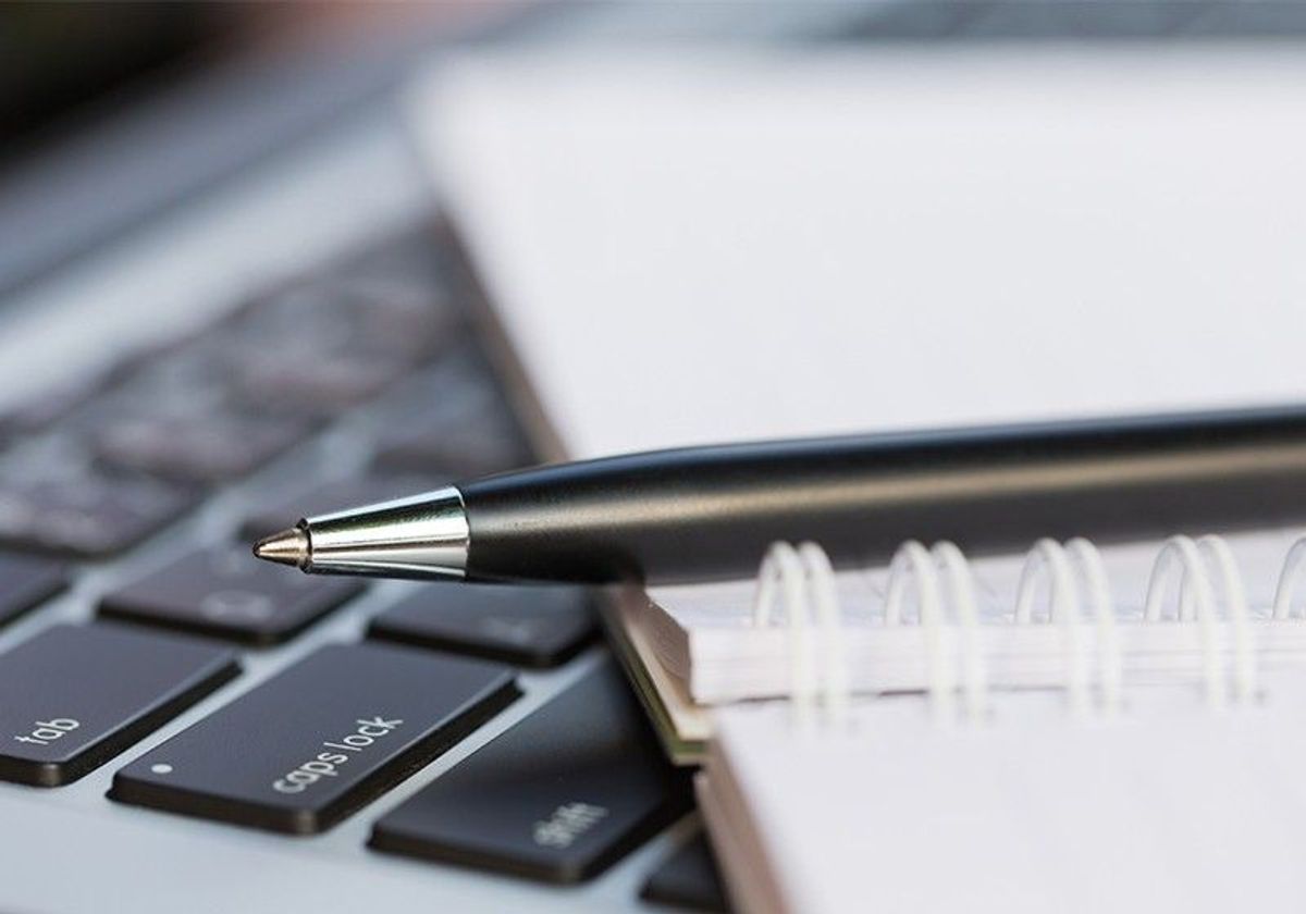 A ballpoint pen placed on top of a notebook that is sitting on top of a laptop keyboard. A ballpoint pen placed on top of a notebook that is sitting on top of a laptop keyboard.