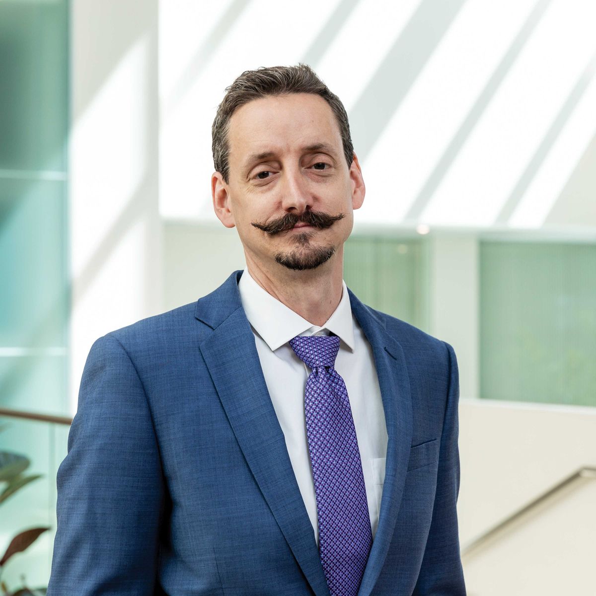 Ian Wickersham wears a collared shirt and a blazer against a white background. Ian Wickersham wears a collared shirt and a blazer against a white background.
