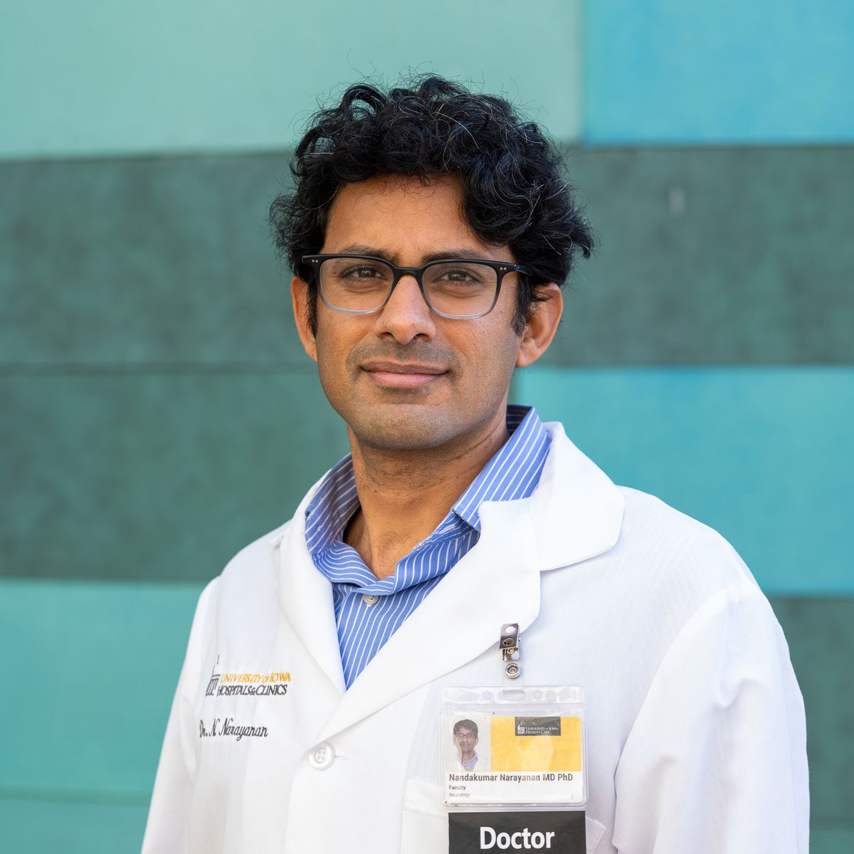 Nandakumar Narayanan wears a lab coat and stands in front of a blue background. Nandakumar Narayanan wears a lab coat and stands in front of a blue background.