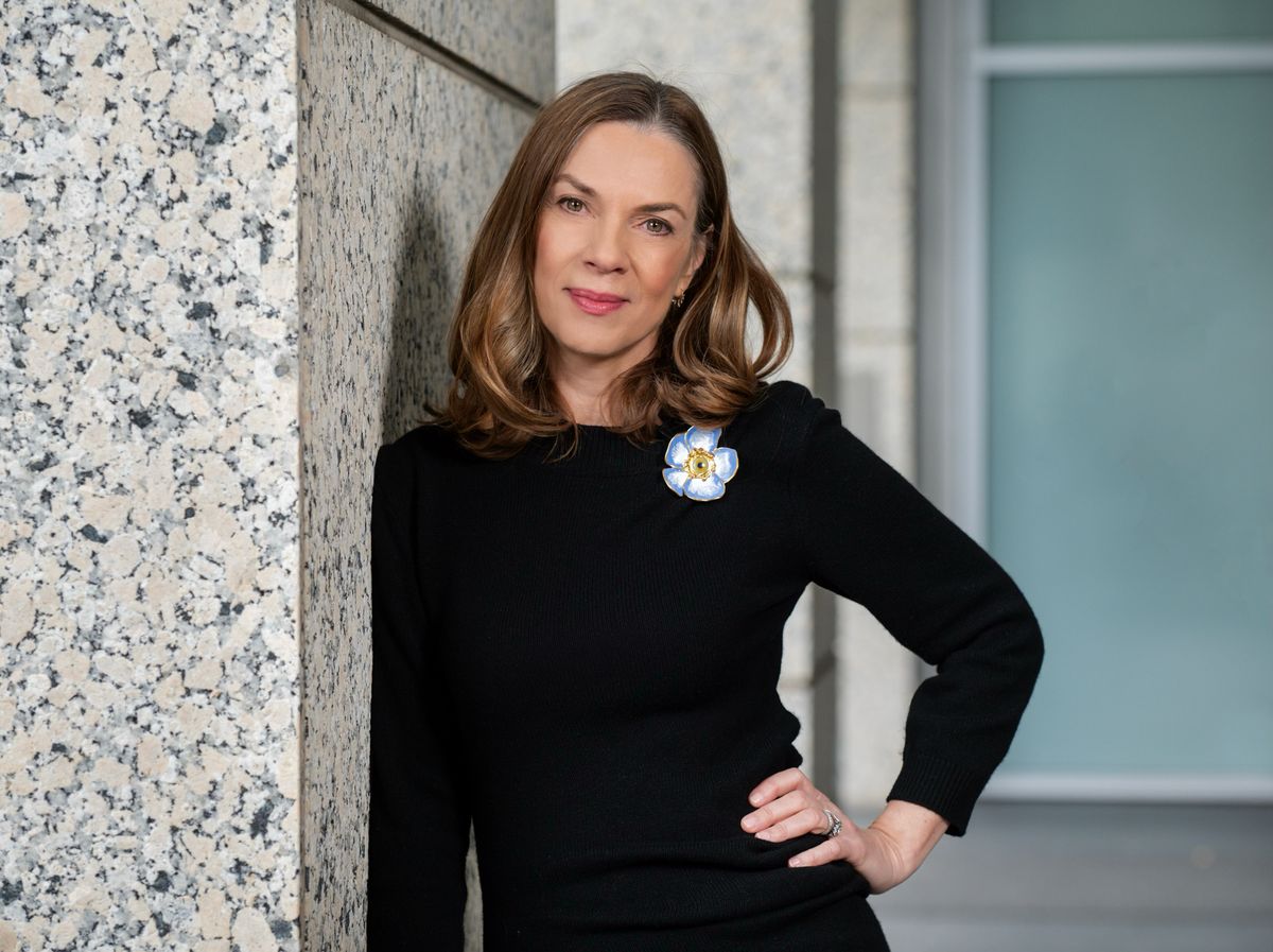 A woman in a black shirt with a flower on it smiles at the camera. A woman in a black shirt with a flower on it smiles at the camera.