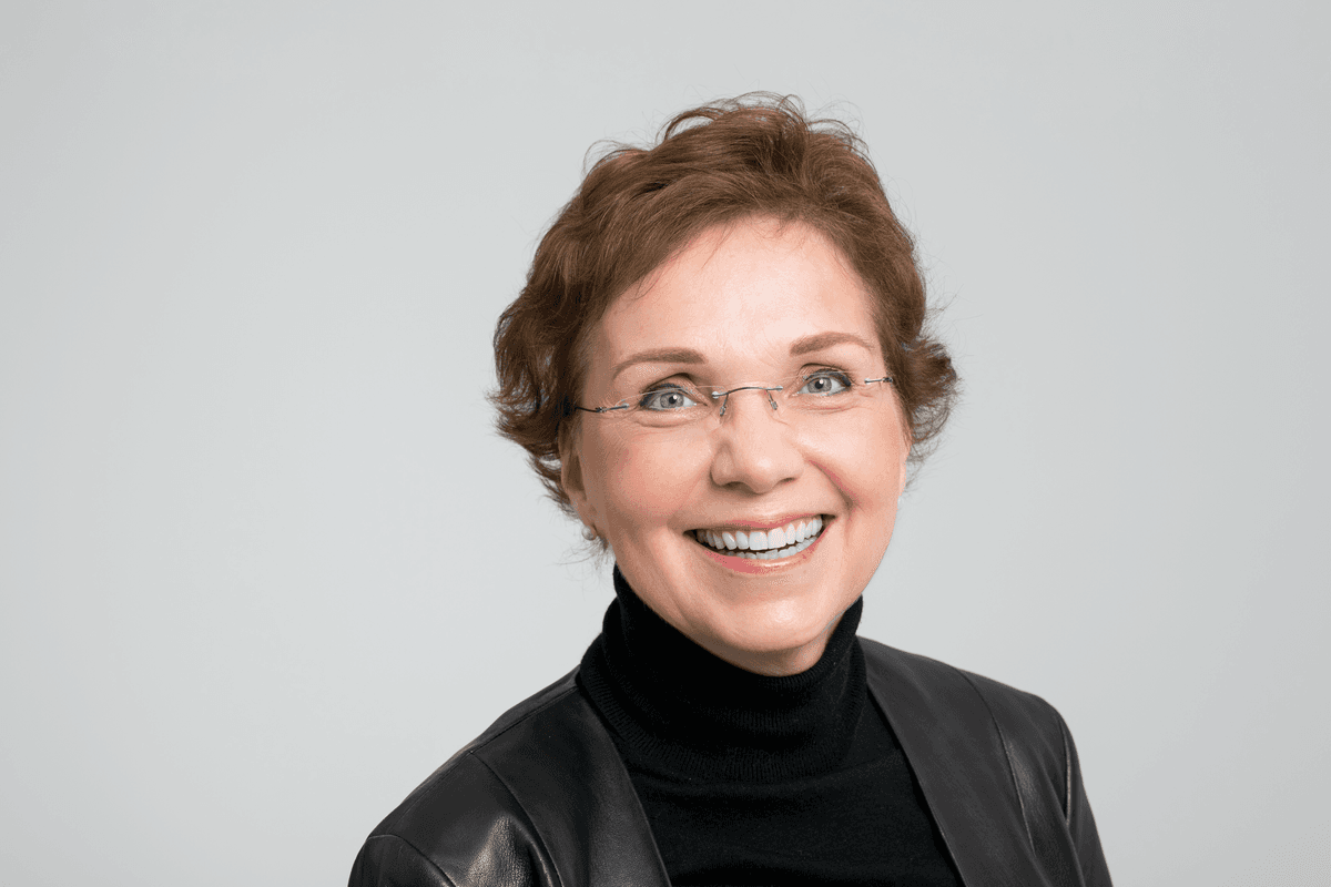 Petra Arck wears a black turtleneck and smiles against a white background. Petra Arck wears a black turtleneck and smiles against a white background.