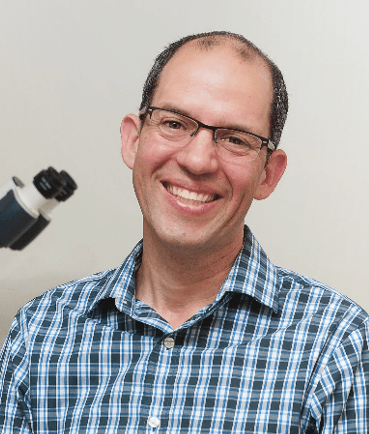 Eytan Wine wears a collared shirt and smiles in front of a microscope. Eytan Wine wears a collared shirt and smiles in front of a microscope.
